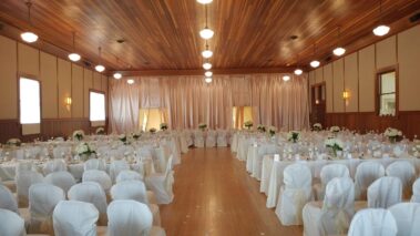 Main hall with white tables and chairs, glassware and white flowers, pink fabric decor on far wall