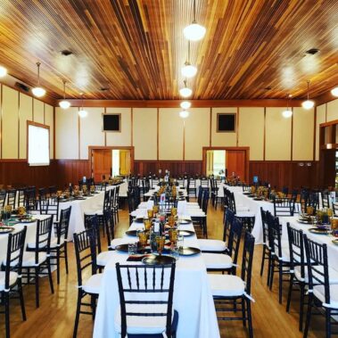 Long shot of wedding in main hall, tables with white cloths, black bamboo chairs and colored glassware