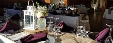 Close up of sunshine on tabletop with white lantern, glassware, flowers and burgundy colored napkins