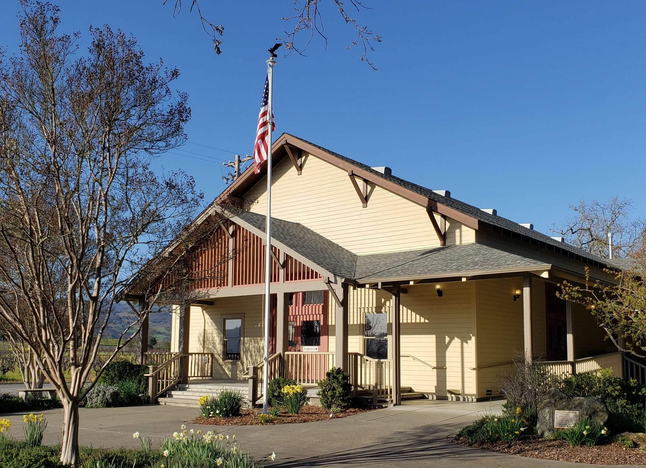 Front view of yellow and brown building with front porch and American flag