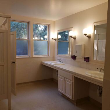 Men's bathroom with white tiled counters, lights on
