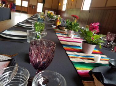Close up of tabletop with black tablecloth, striped runner, colored goblets and potted flowers